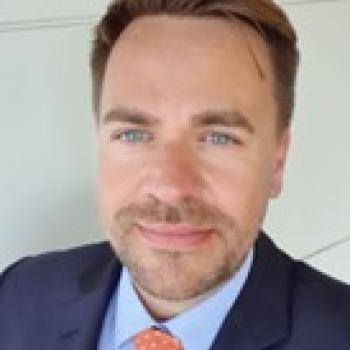 A man wearing a suit and tie in a headshot 