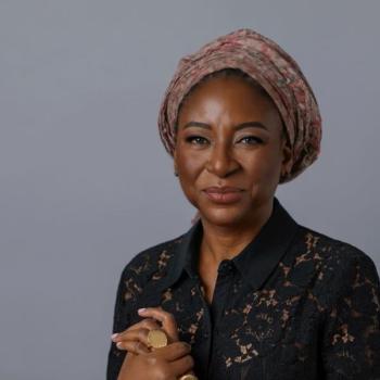 woman in black and a patterned head scarf smiles towards the camera