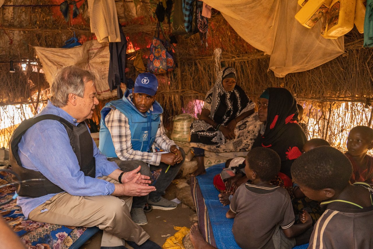 group of people sit inside a hut speaking 