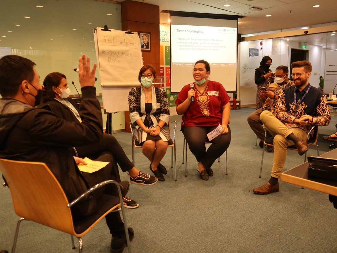 Five persons talking while sitting in chairs in a circle with a flipchart to their side