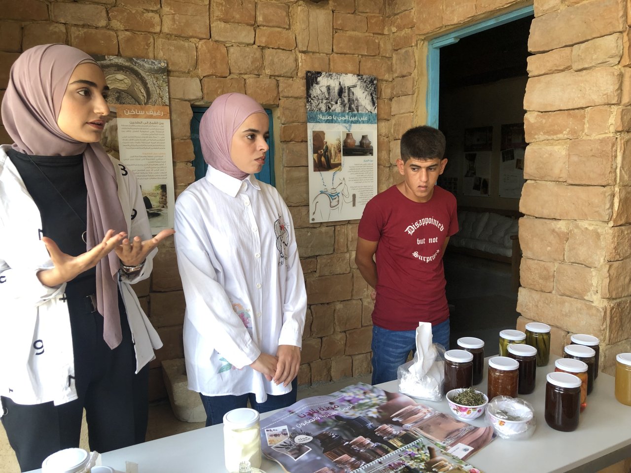 two young woman and a man stand behind stall showing their products