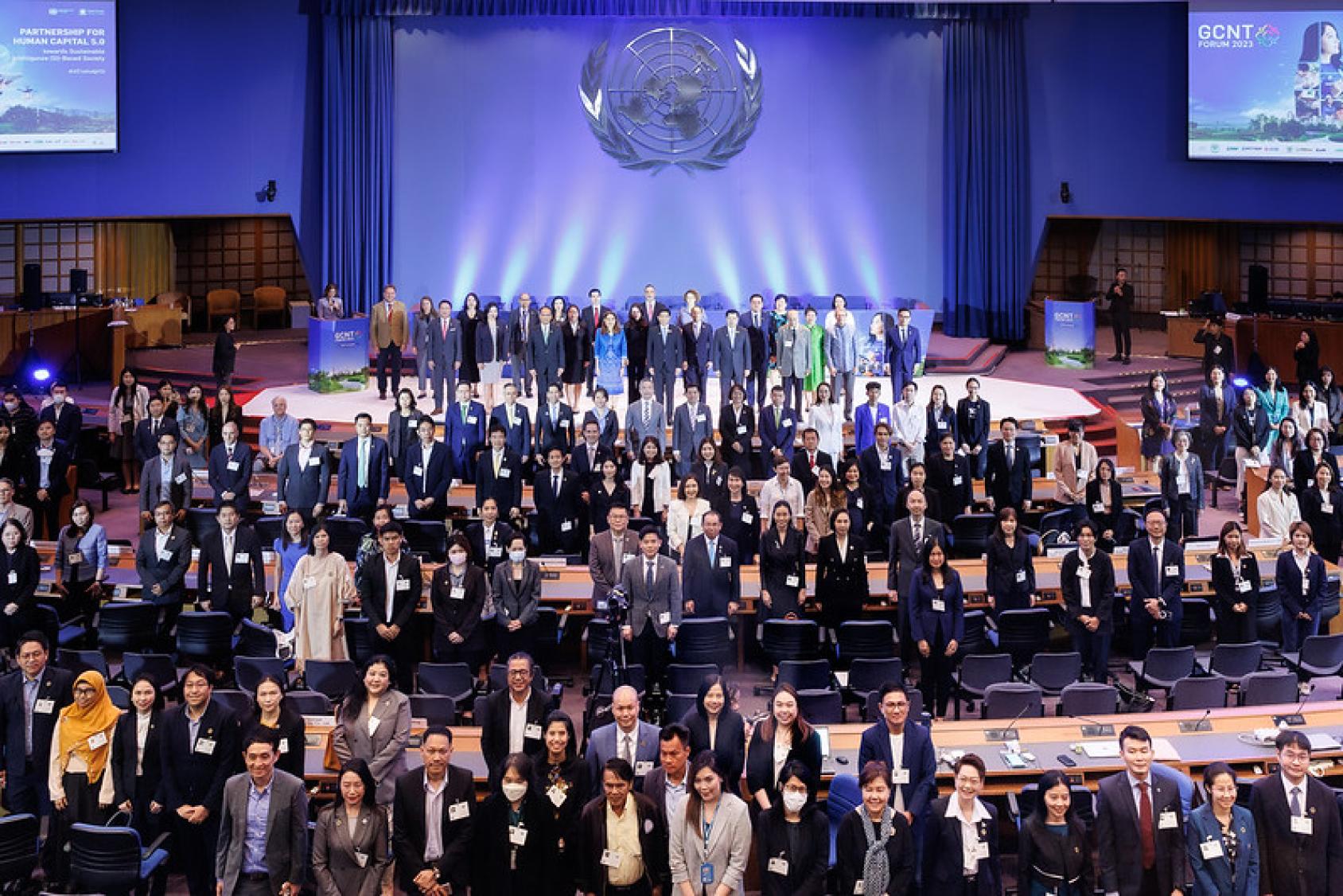 A large group of people, mostly wearing suits and formal attire are in an auditorium with the UN logo in the background