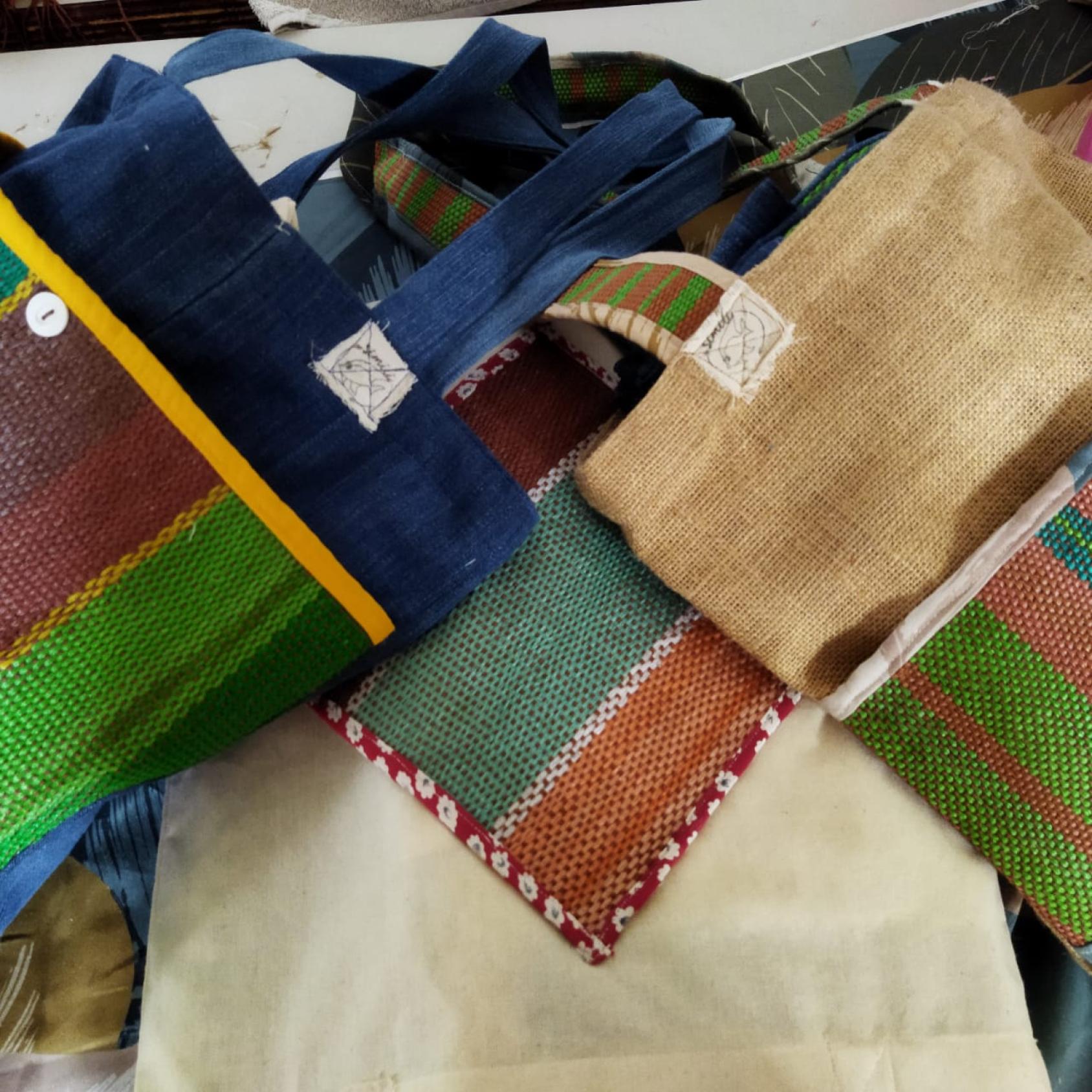 A collection of colorful handcrafted bags made from different fabrics. The bags feature a variety of textures and patterns, including stripes and checks. Some have additional details like buttons and embroidered patches. The image showcases the intricate workmanship and diversity in design of these fabric bags, highlighting the artistry in textile crafts.