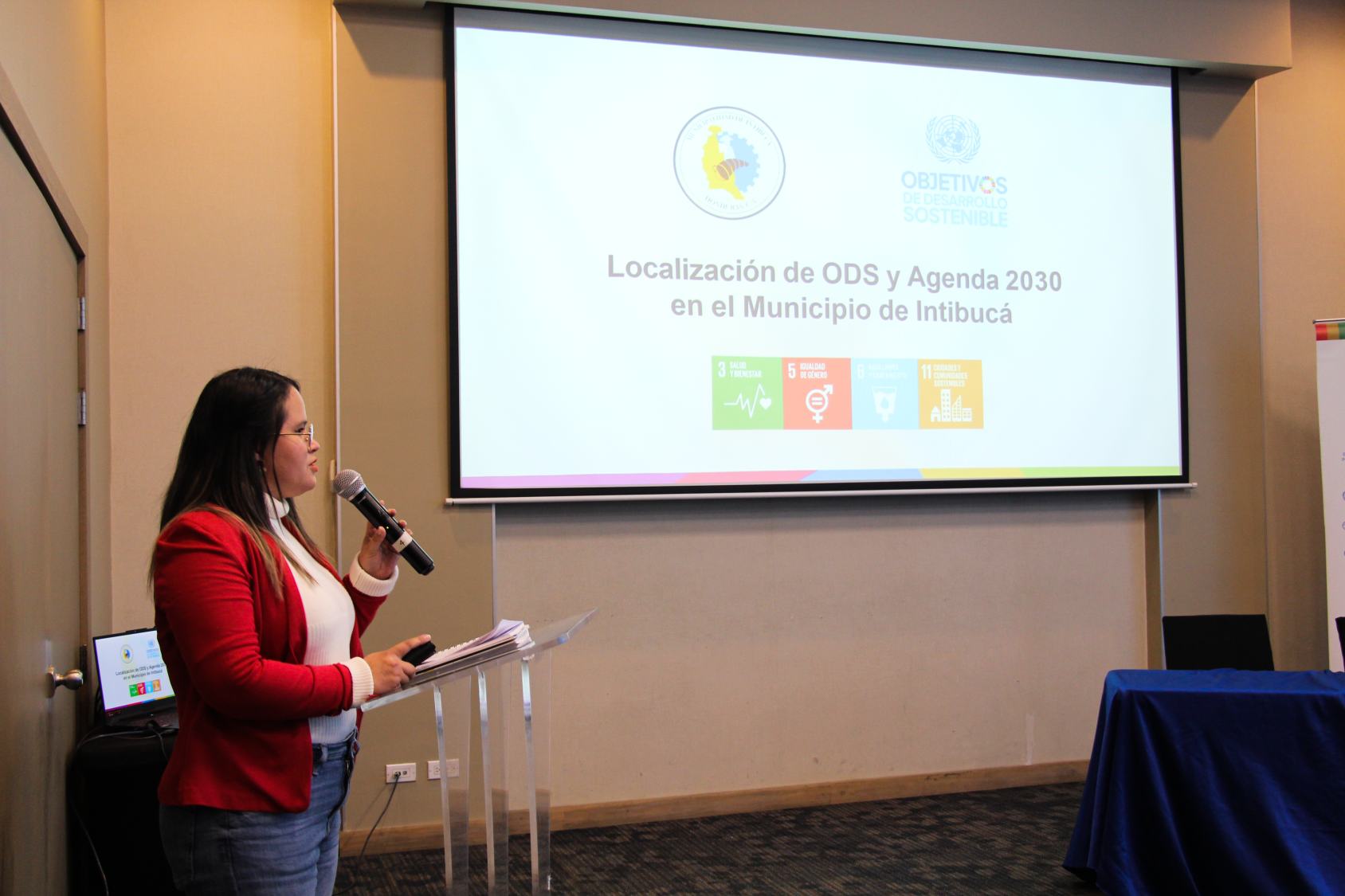 A woman stands in front of a screen explaining to an audience