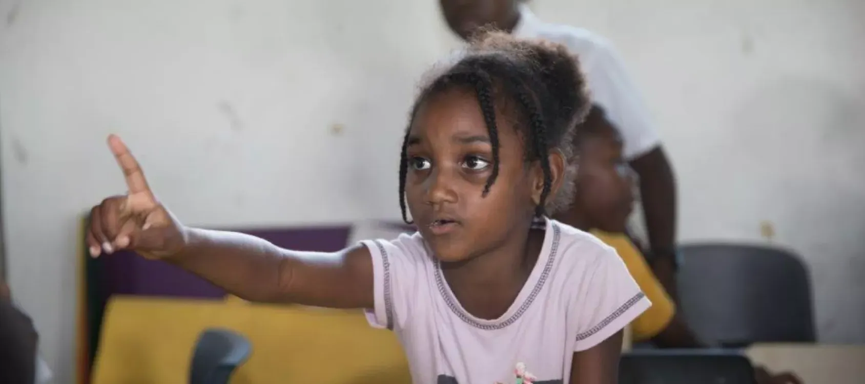 A young girl raises her hand in a classroom