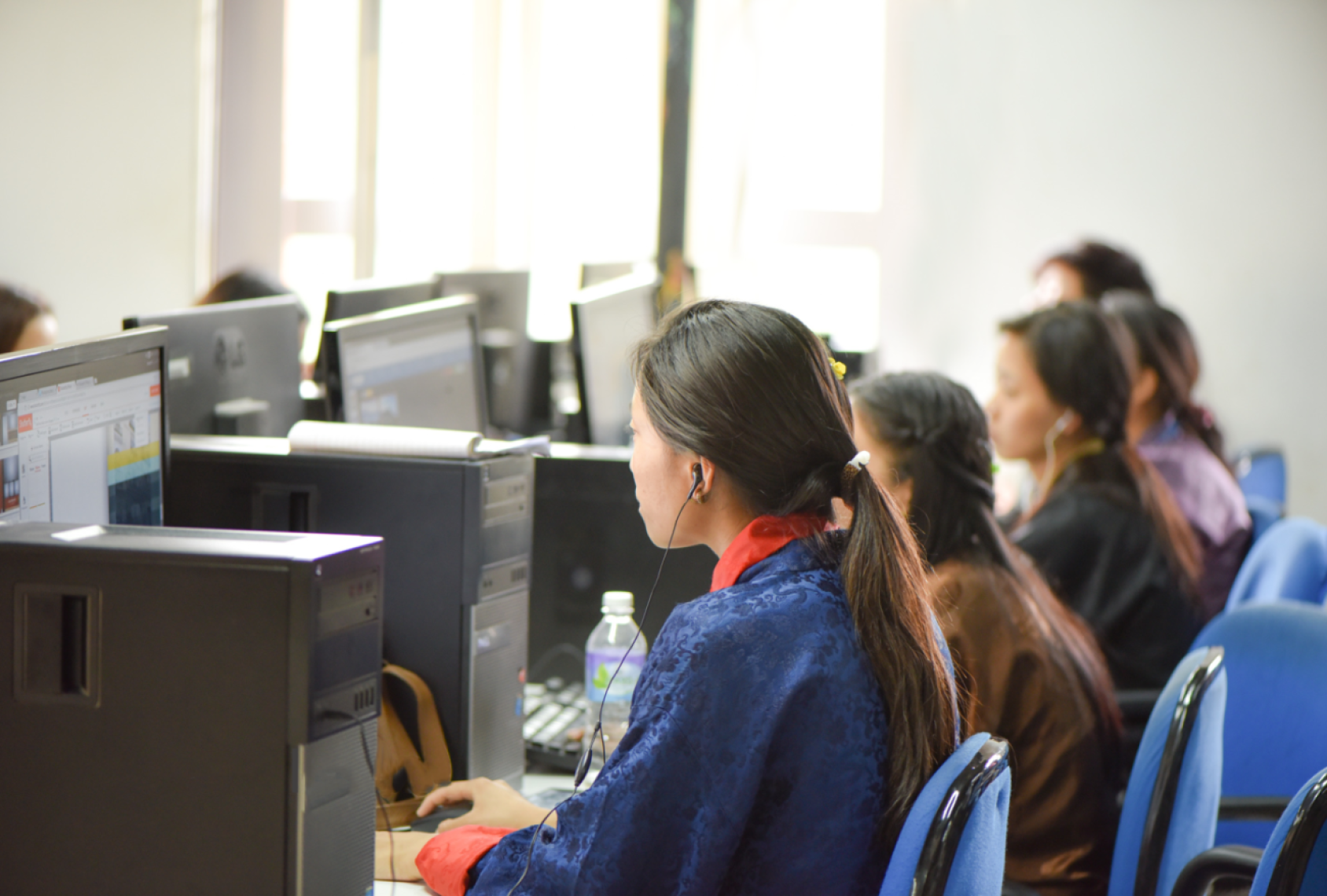 A young girl looking at a computer screen, he back is turned to the camera