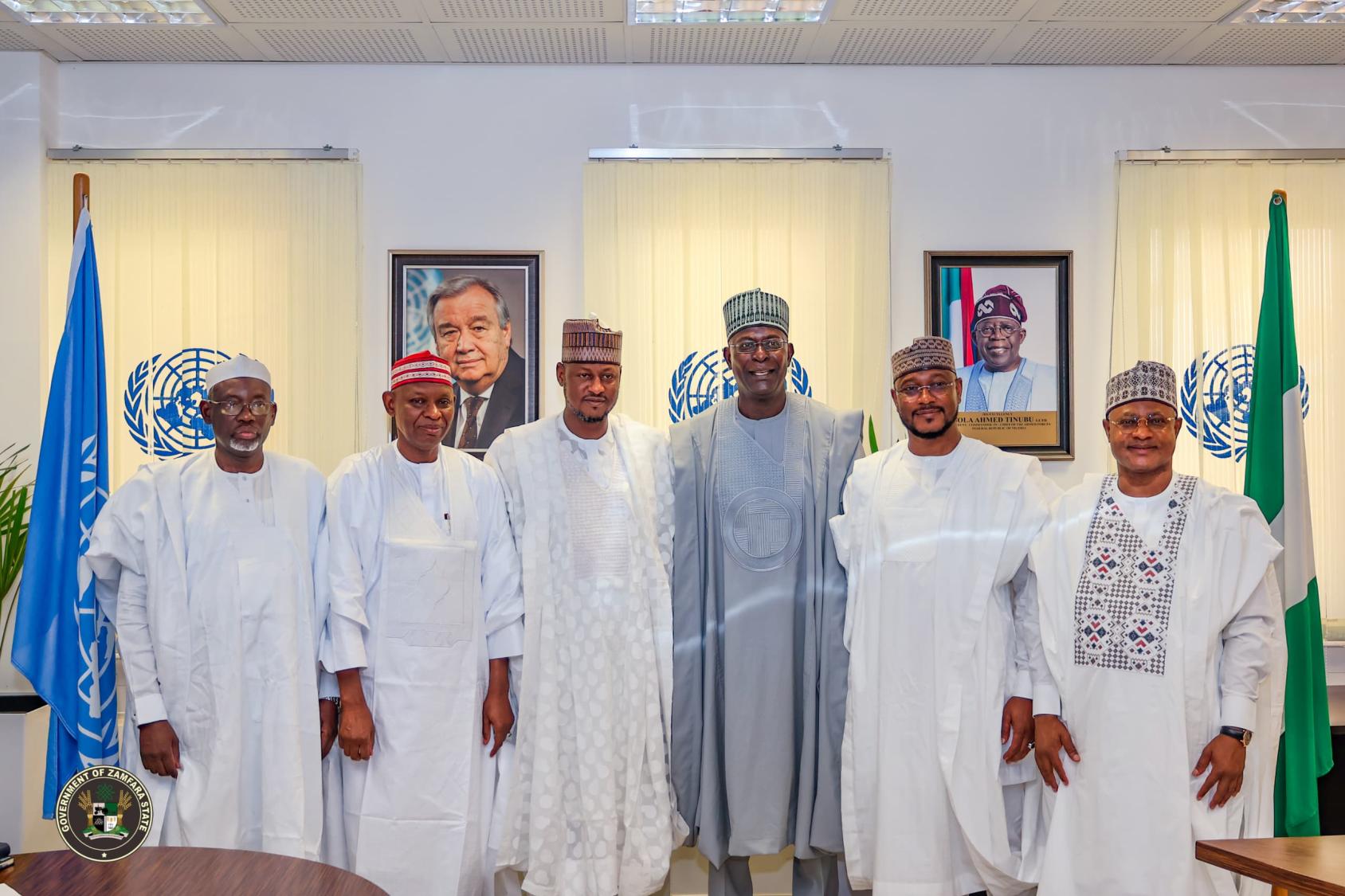 A group of men dressed in traditional African dress, standing in front of flags of the UN  and Nigeria 