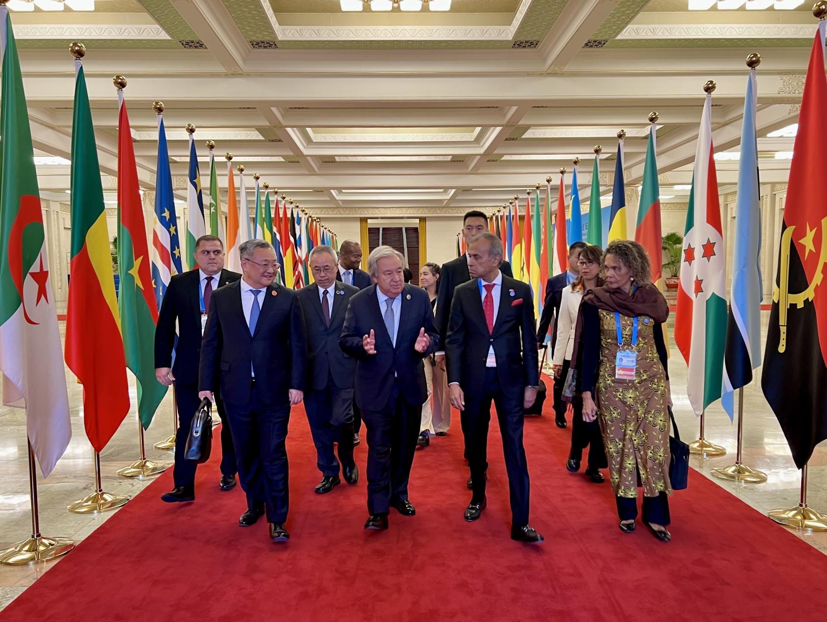 A group of people walk down a long hallway with flags on the two sides