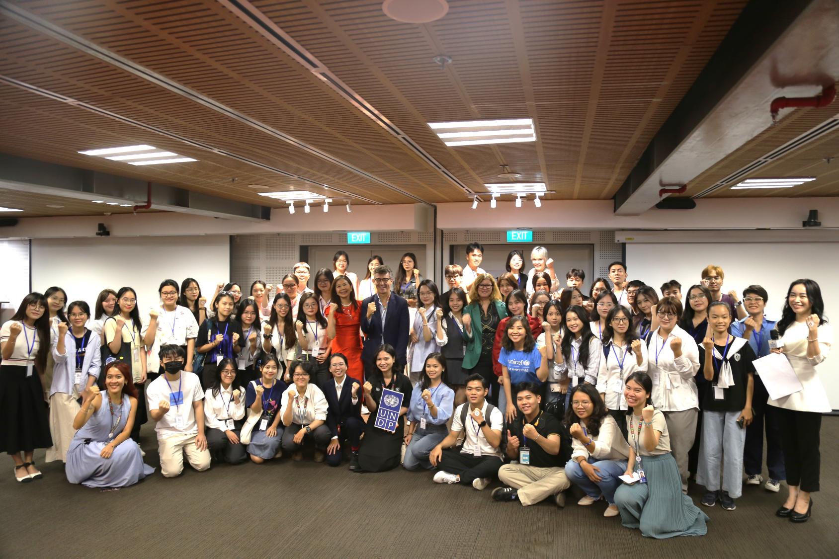 A group of young people in a conference room huddled together and smiling at the camera