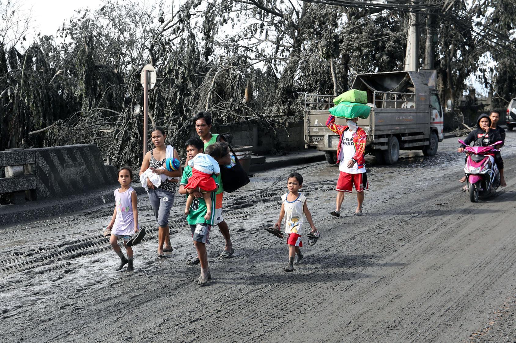 A family affected by the eruption of the Taal volcano in 2020 walks in volcanic ash-covered streets.