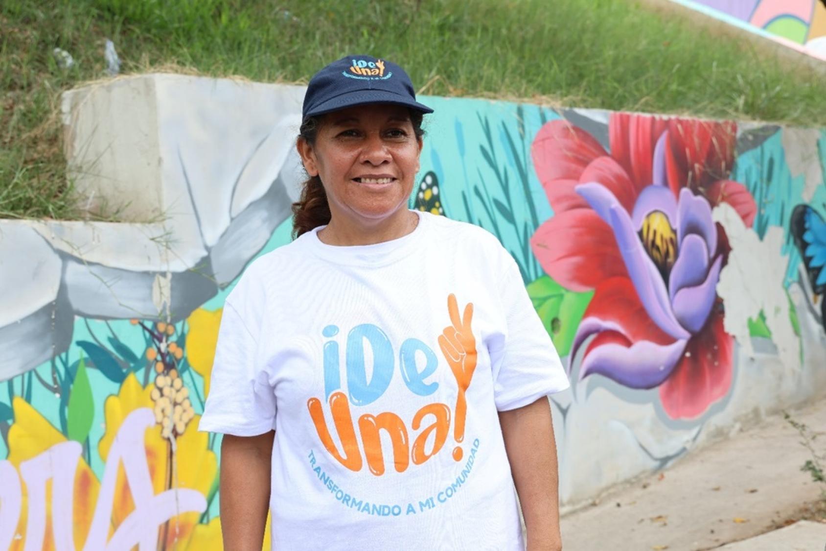 A young woman wearing a t-shirt that reads Del Una and standing in front of a colourful wall