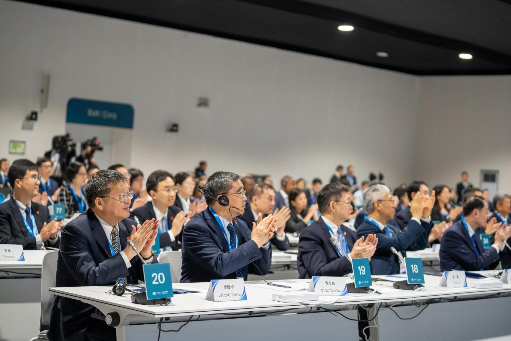 A group of people are in a conference room indoors wearing suits