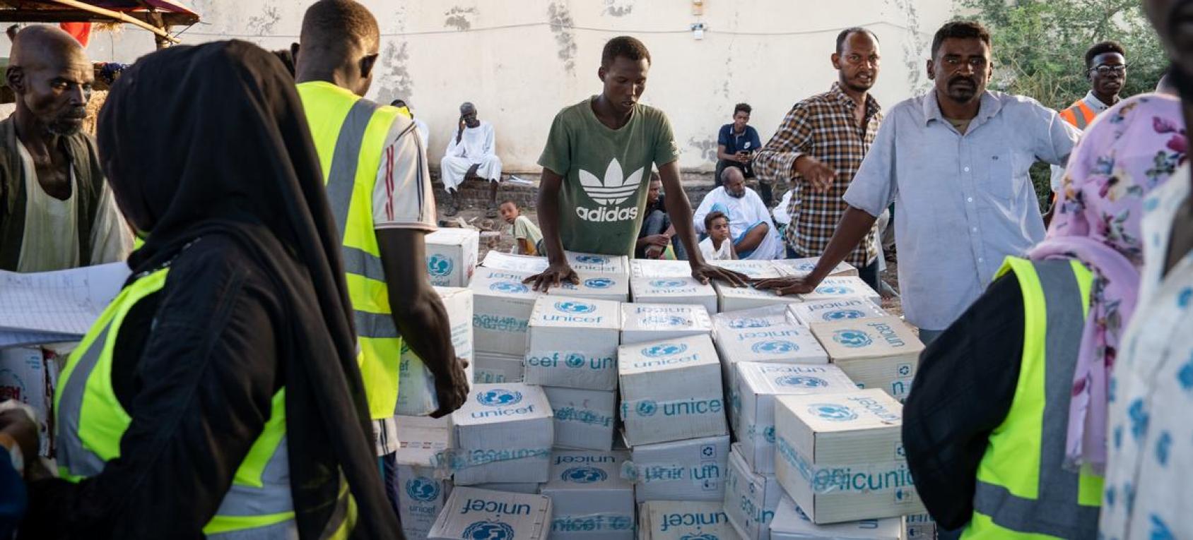 A group of people standing around boxes of supplies marked with UNICEF branding