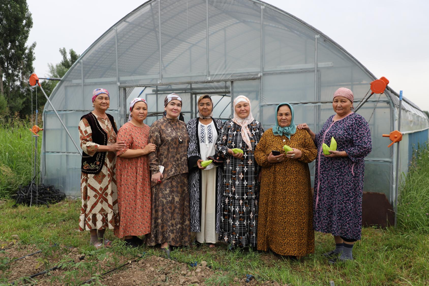 A group of women standing outdoors holding agricultural produce 