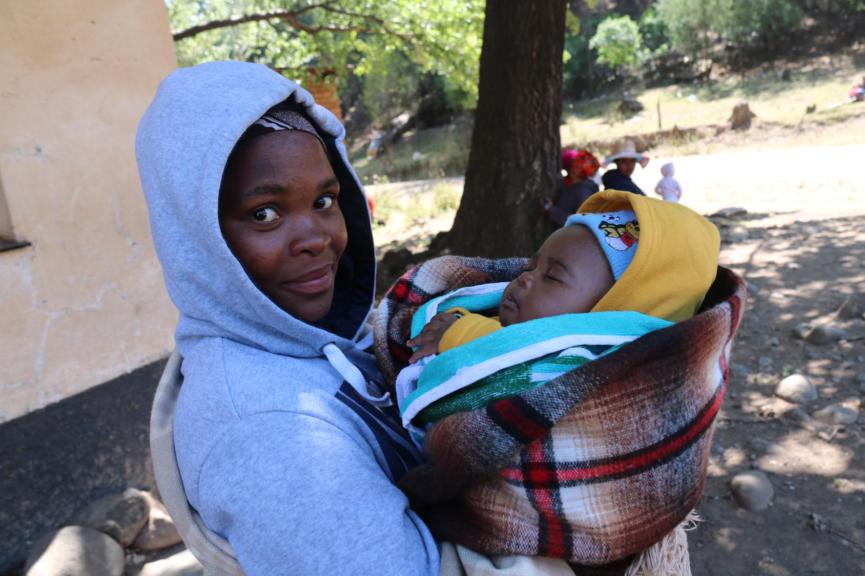 A woman is holding her baby and looking at the camera