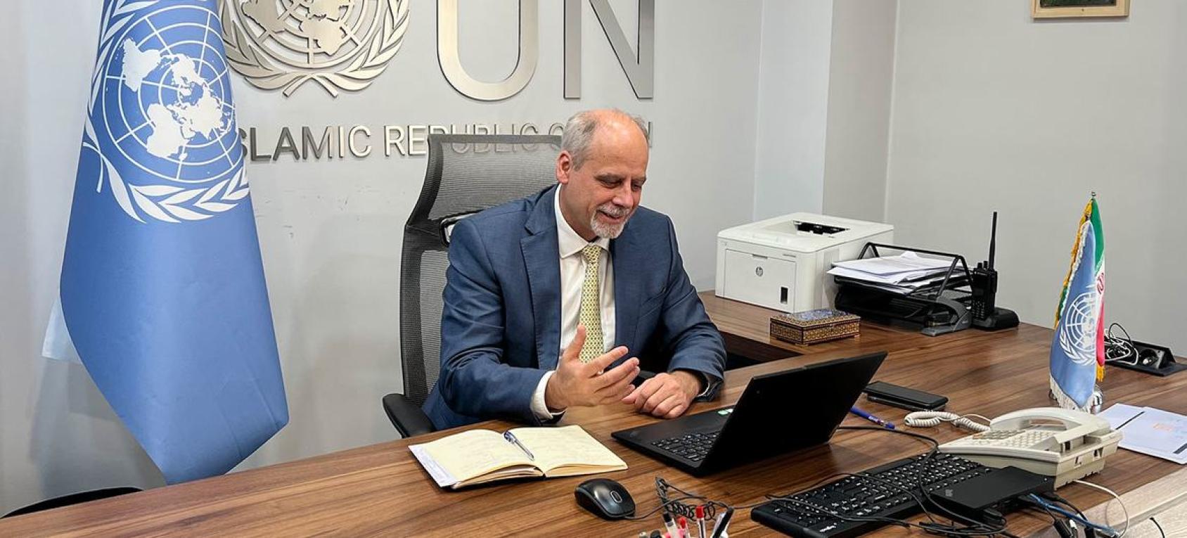 UN Resident Coordinator sits at a desk with the UN flag behind him
