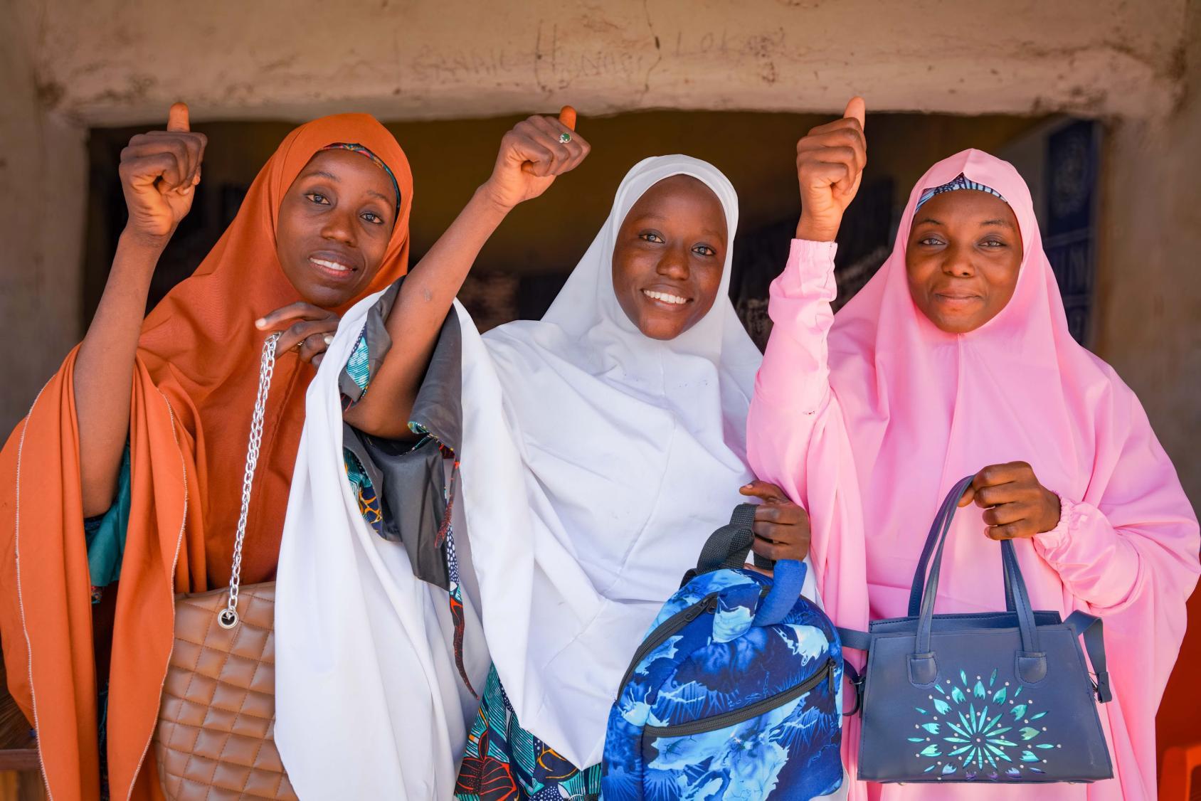 A group of young women looking at the camera holding bags and making a positive hand up gesture