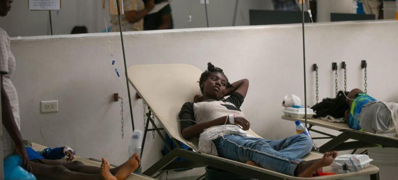 A woman lays on a cot near medical equipment.