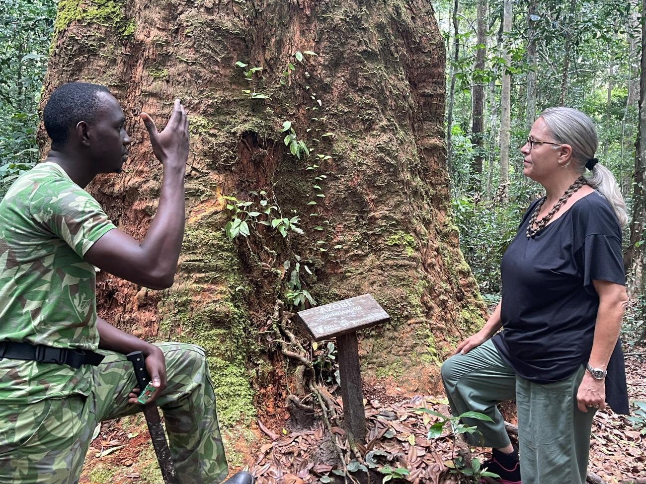 Two people speak near a tree.