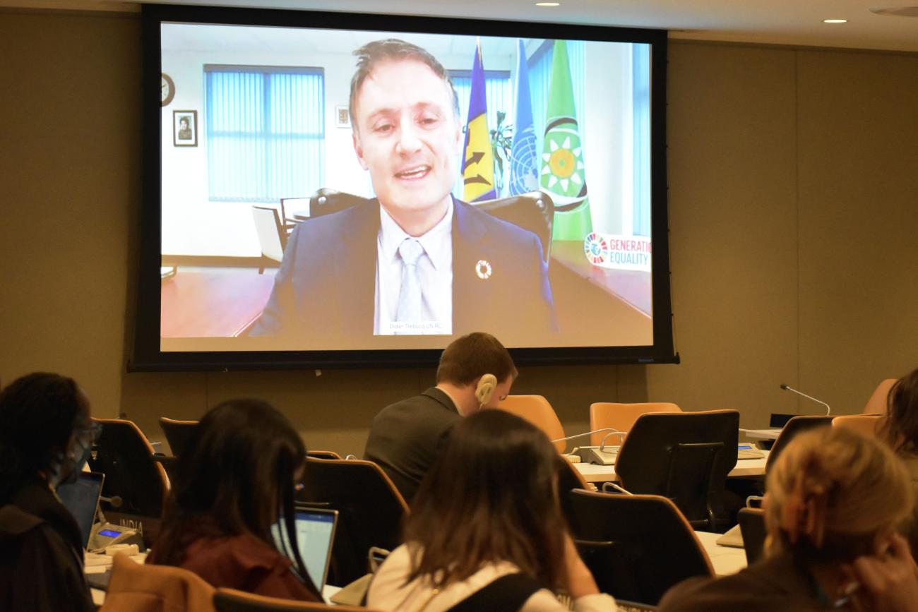 Man on screen speaks to a group of people at a meeting 