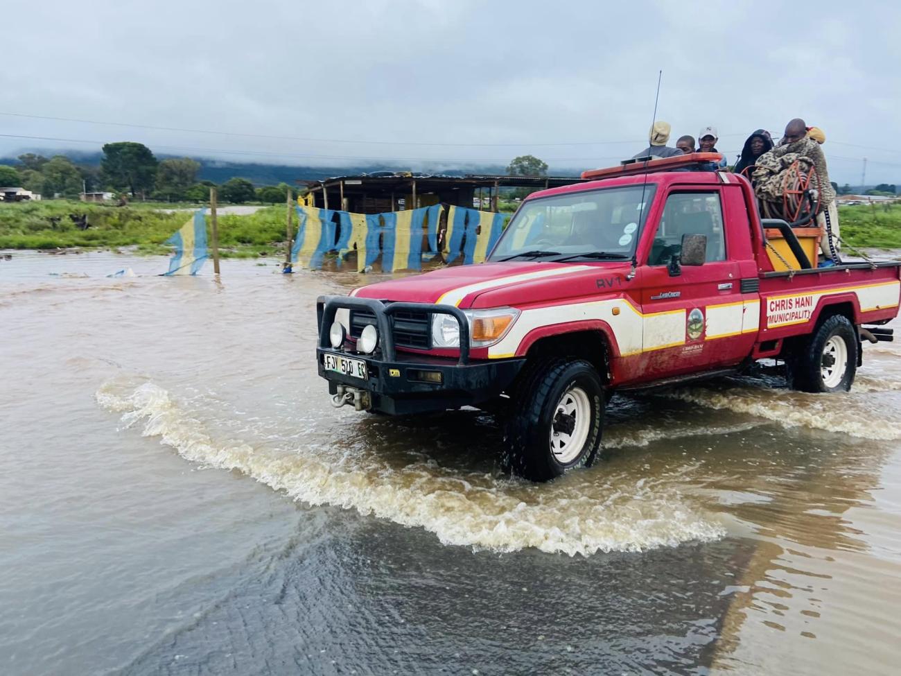 a red truck driving along a flooded road 