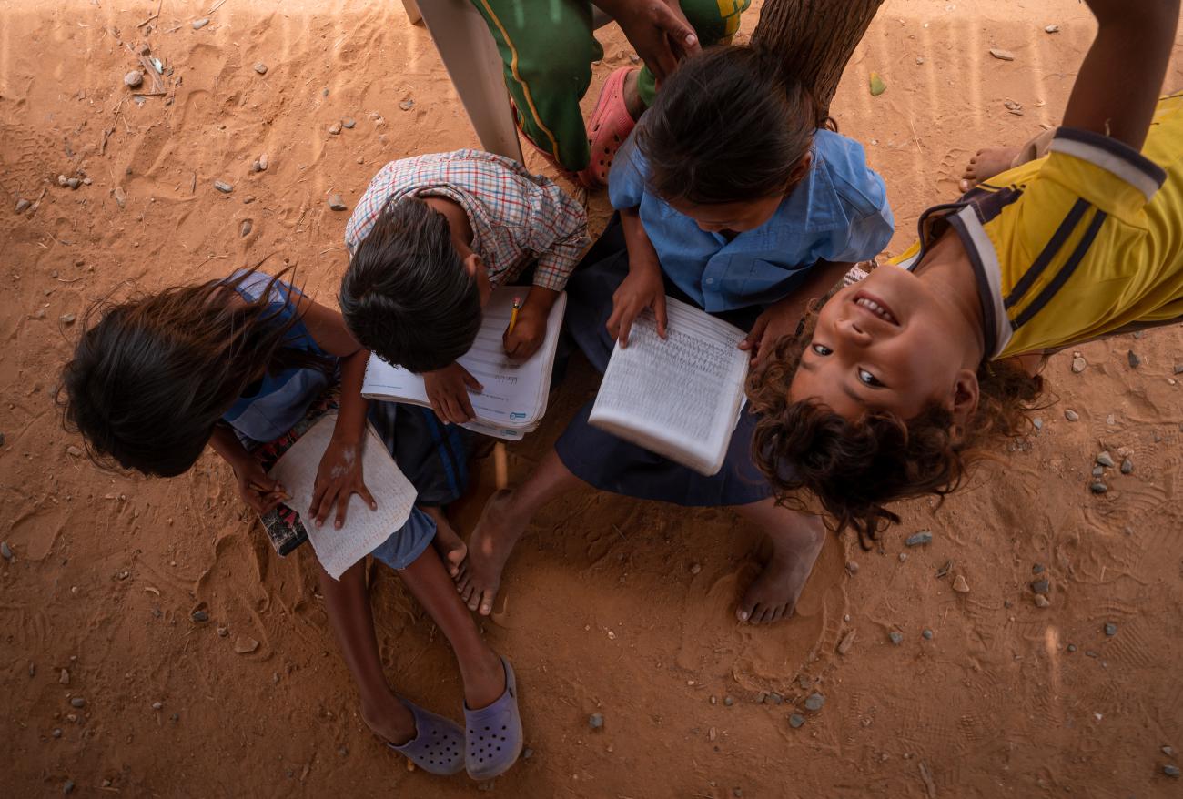 group of young children sit on the ground with paper and pens 