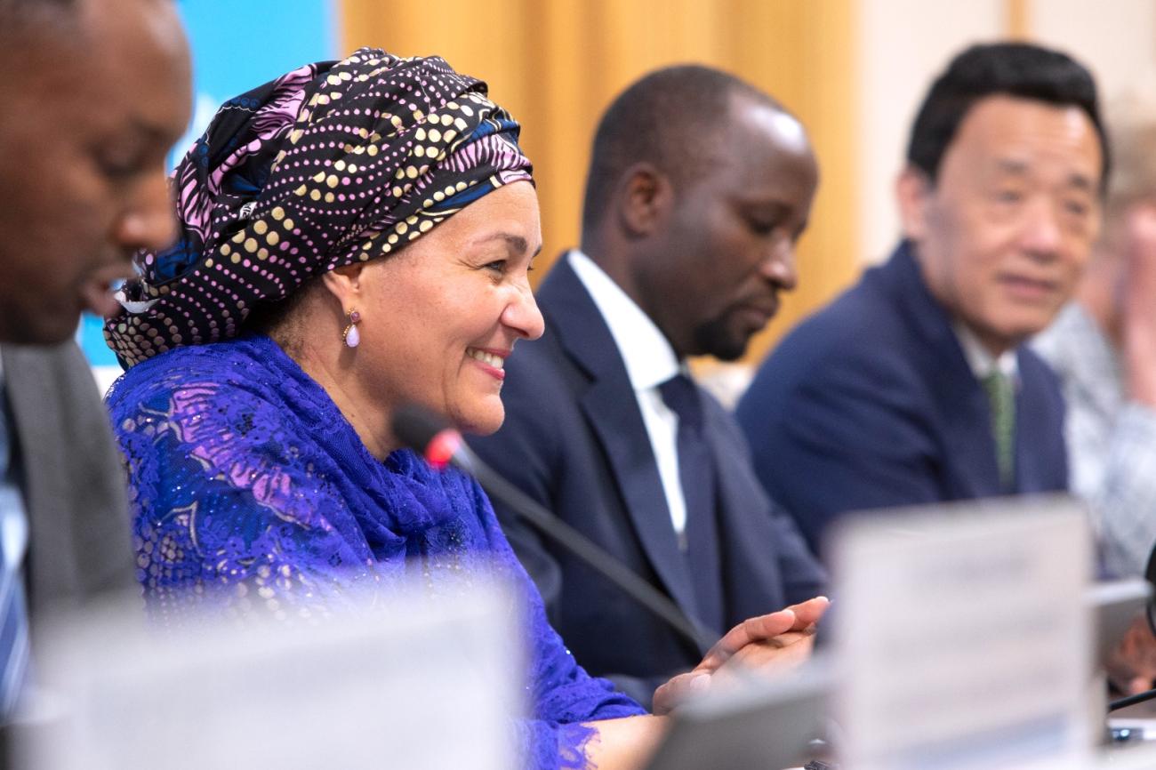 woman in blue top and dark head scarf smiles while sitting alongside other people at panel discussion 