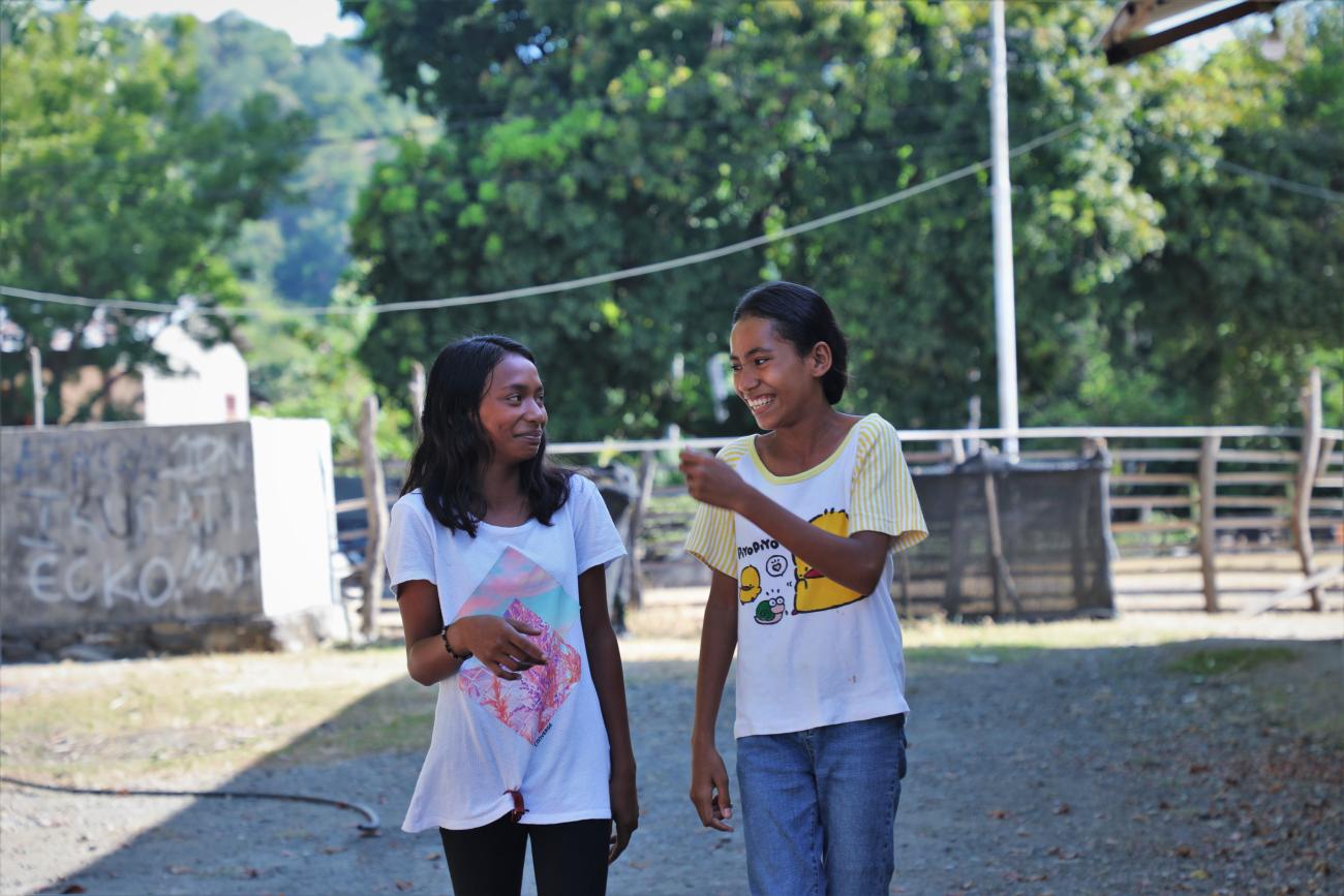 Two young girls speak to each other outside with trees in the background 