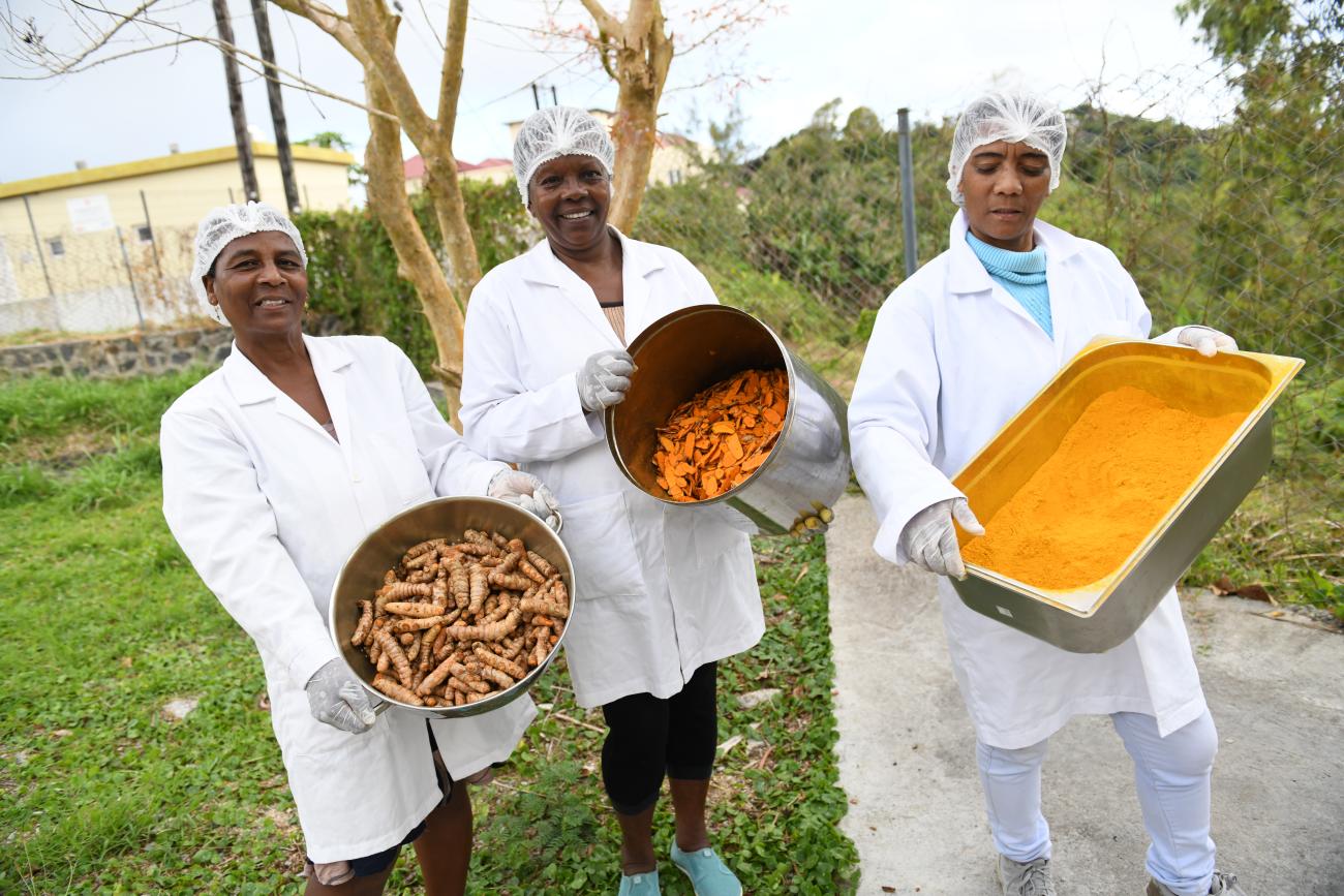 three women in white coats hold pans with food 