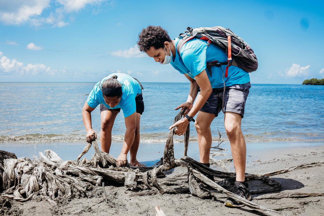 two people in blue t-shirts bend down to collect litter from the beach