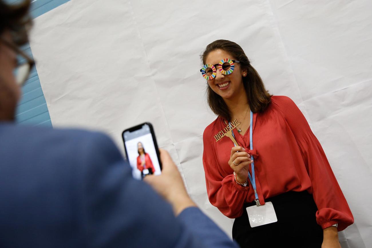 young woman in red shirt poses for a photo in SDG themed glasses