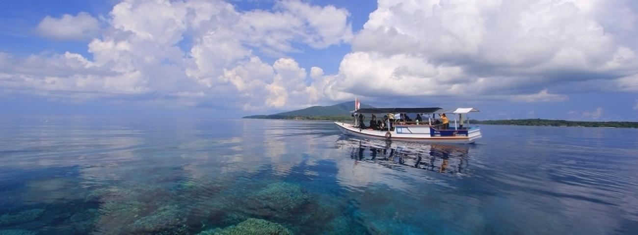 A small white boat with people sails over crystal blue waters in Indonesia