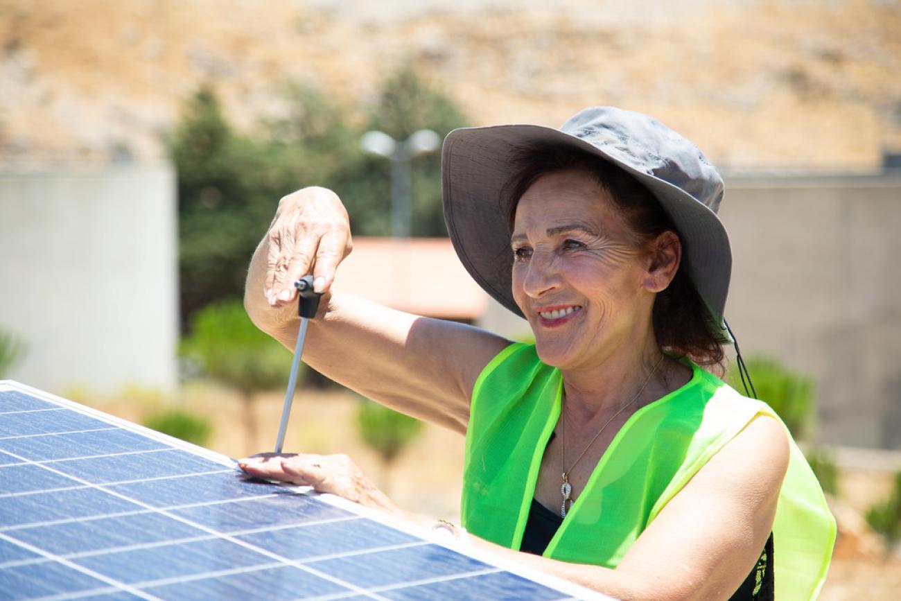 woman with hat and green vest fixes a solar panel 