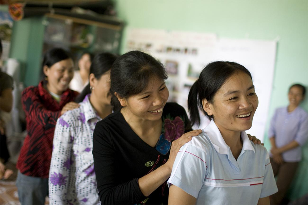 women standing in a line behind each other laugh and smile 