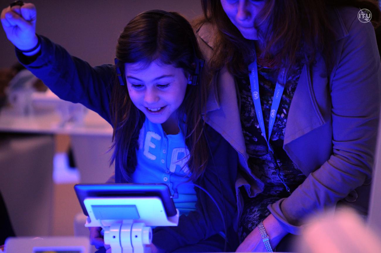 Young girl reaches her hand into the air while looking down at a tablet