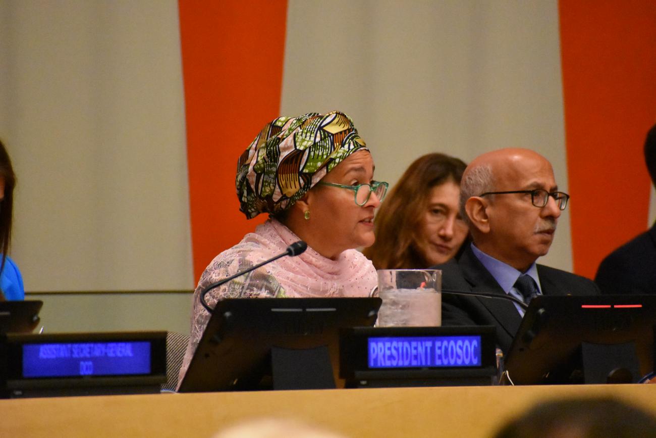 Woman in pink top and patterned headscarf speaks into microphone at panel discussion