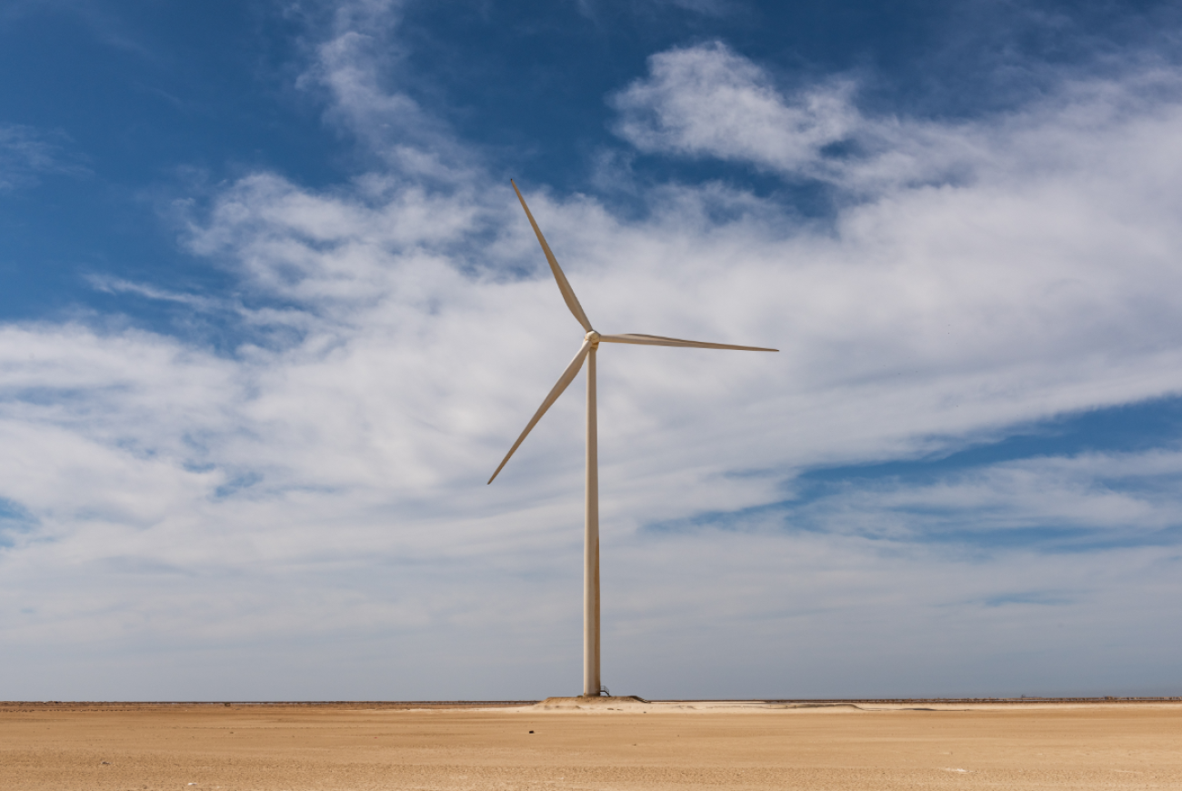 a wind turbine in a field against cloudy blue sky 