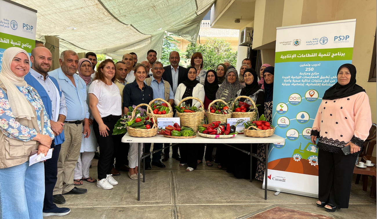 group of people pose for a photo standing around a table of fruit and vegetables