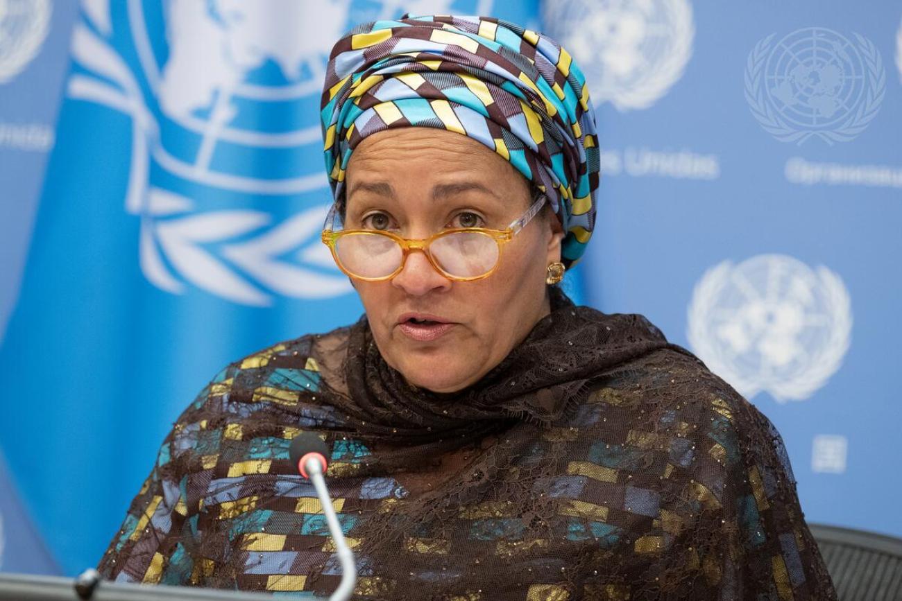 woman in colourful headscarf speaks into microphone against blue background