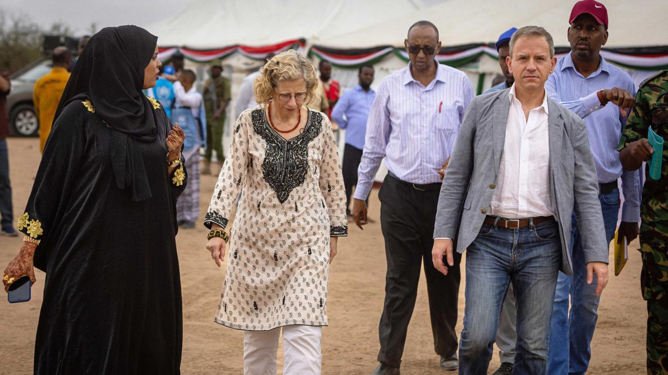 man and woman walk towards camera in outdoor camp, with other people walking alongside them