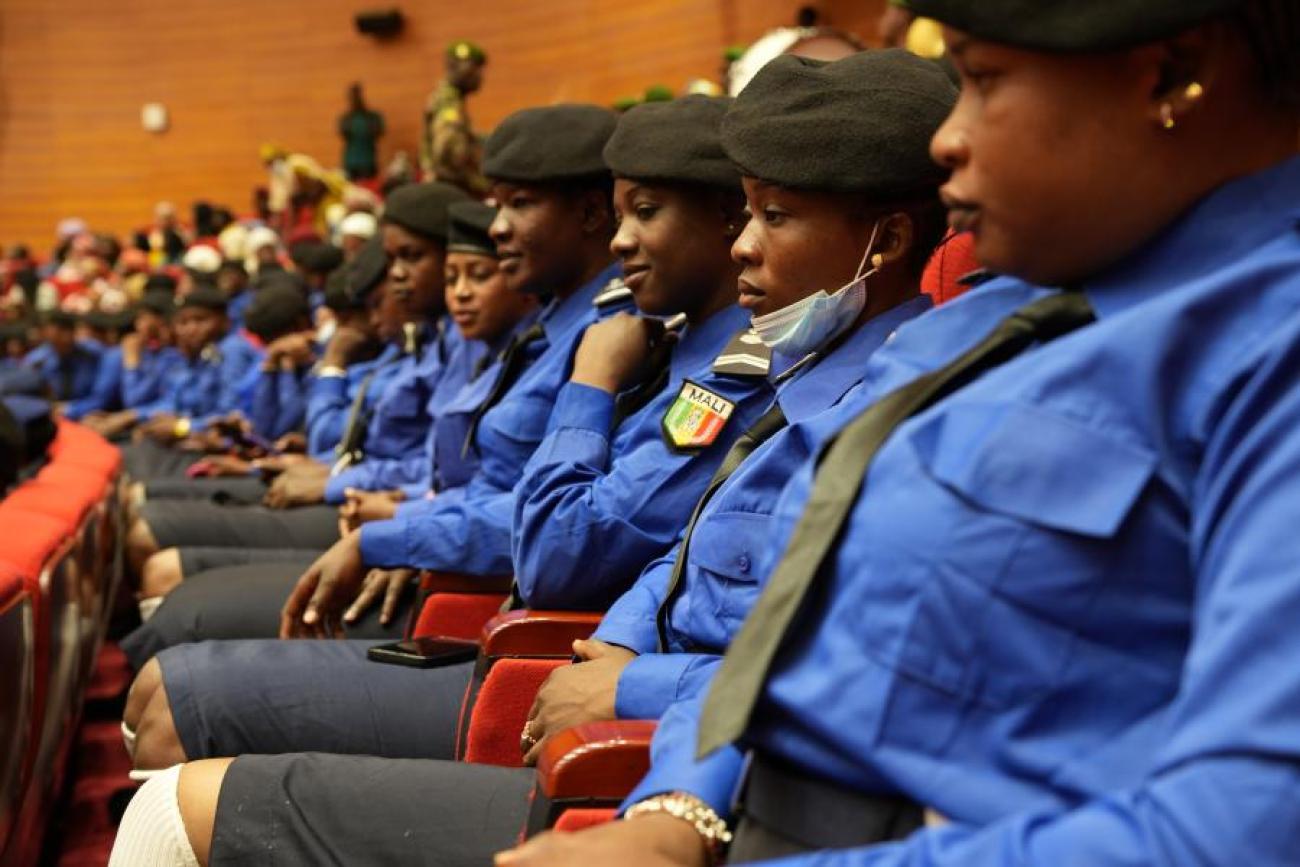 Women police officers seated indoors at a ceremony. They are wearing uniforms of blue shirts, grey shorts and hats