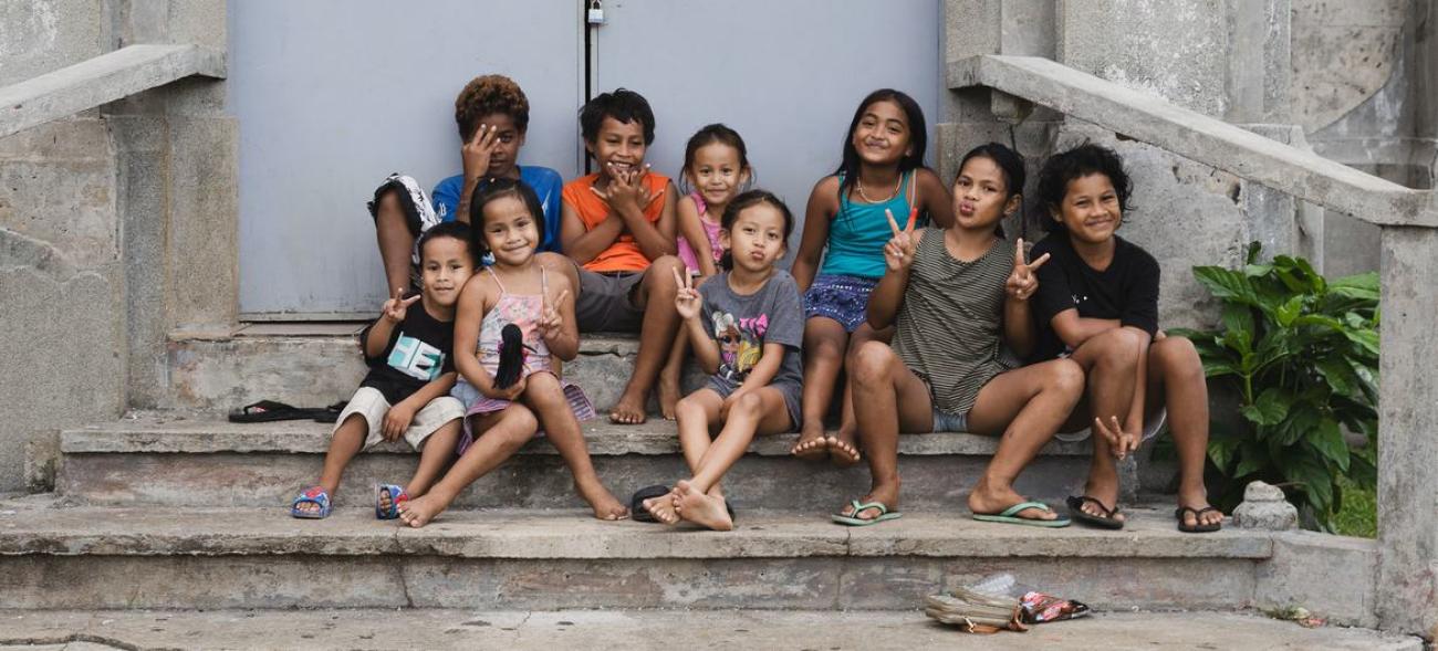 A group of children in colourful clothes sit on the steps, smiling to the camera