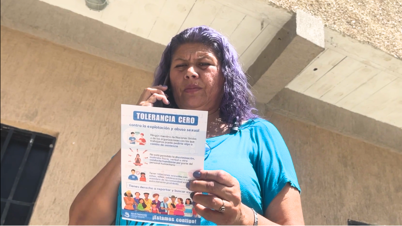 A woman in a blue shirt with purple hair calls someone on her mobile phone while reading a pamphlet