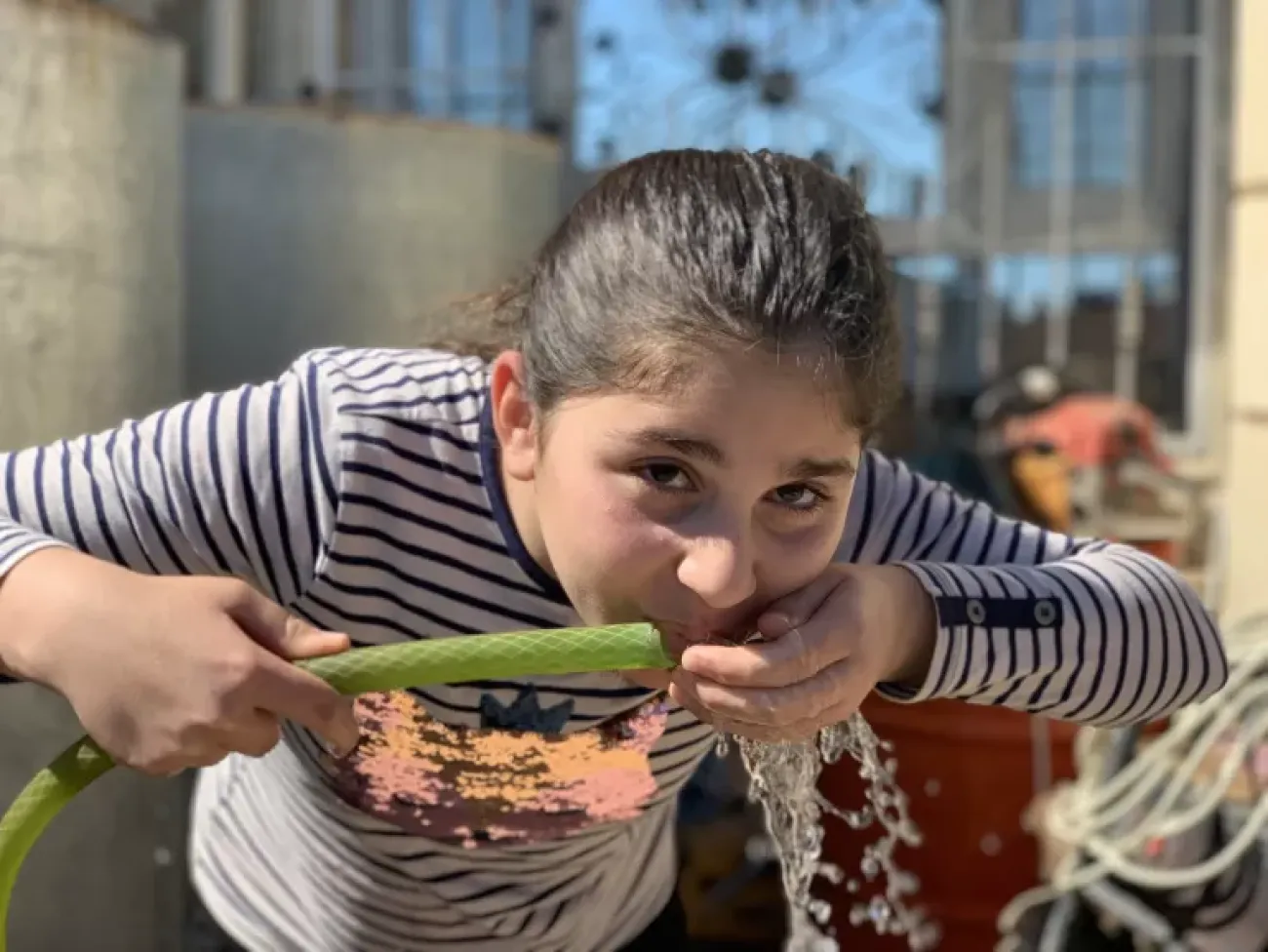 A young girl outdoors drinking water from a tube