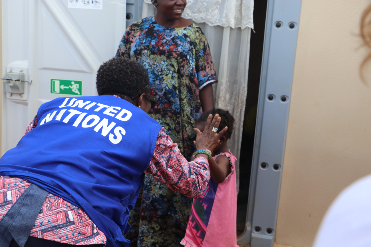 A woman bends over and gives a high-five to a child, she is wearing a blue vest that reads 'United Nations'