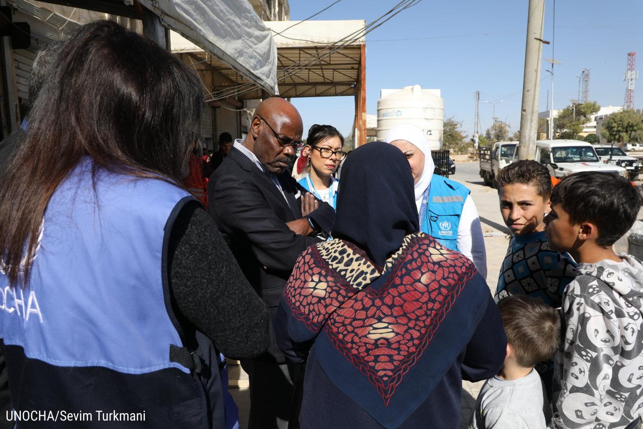 The Resident Coordinator is standing in the middle of a group of people and listening to them