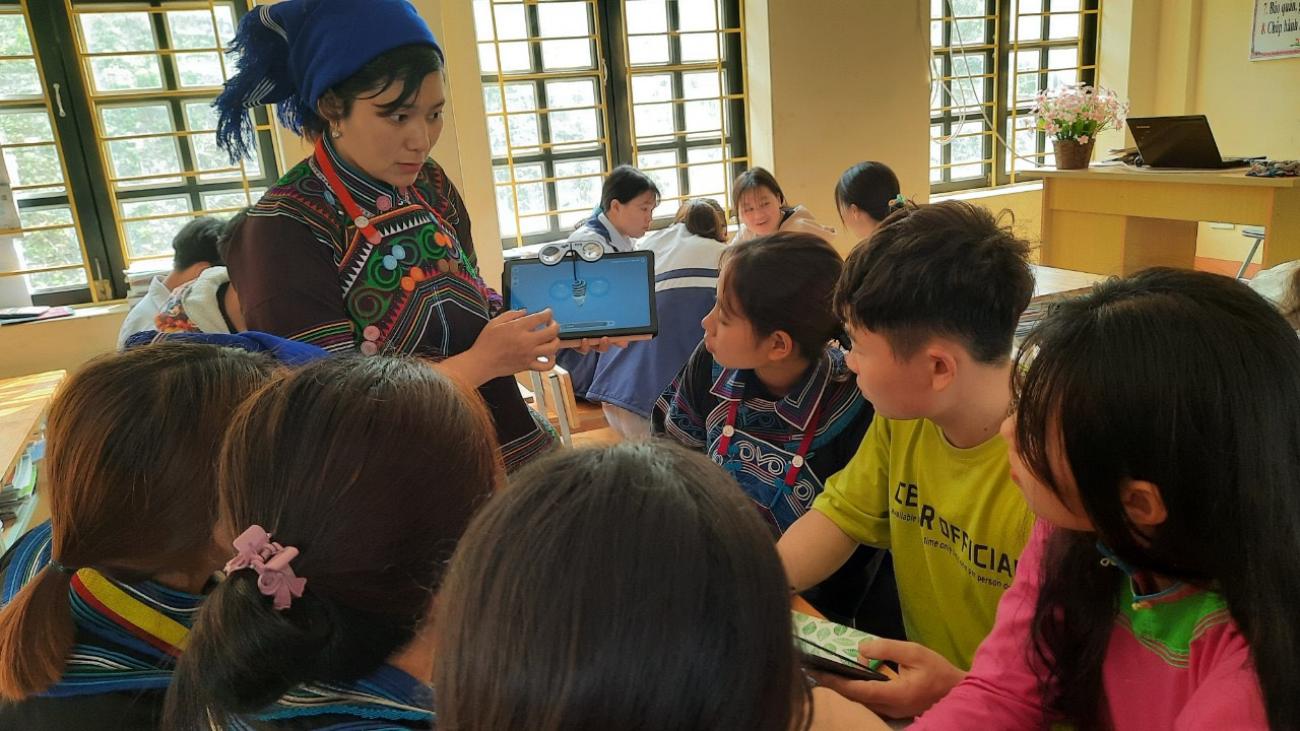 A teacher holds a tablet in front of her students in a classroom