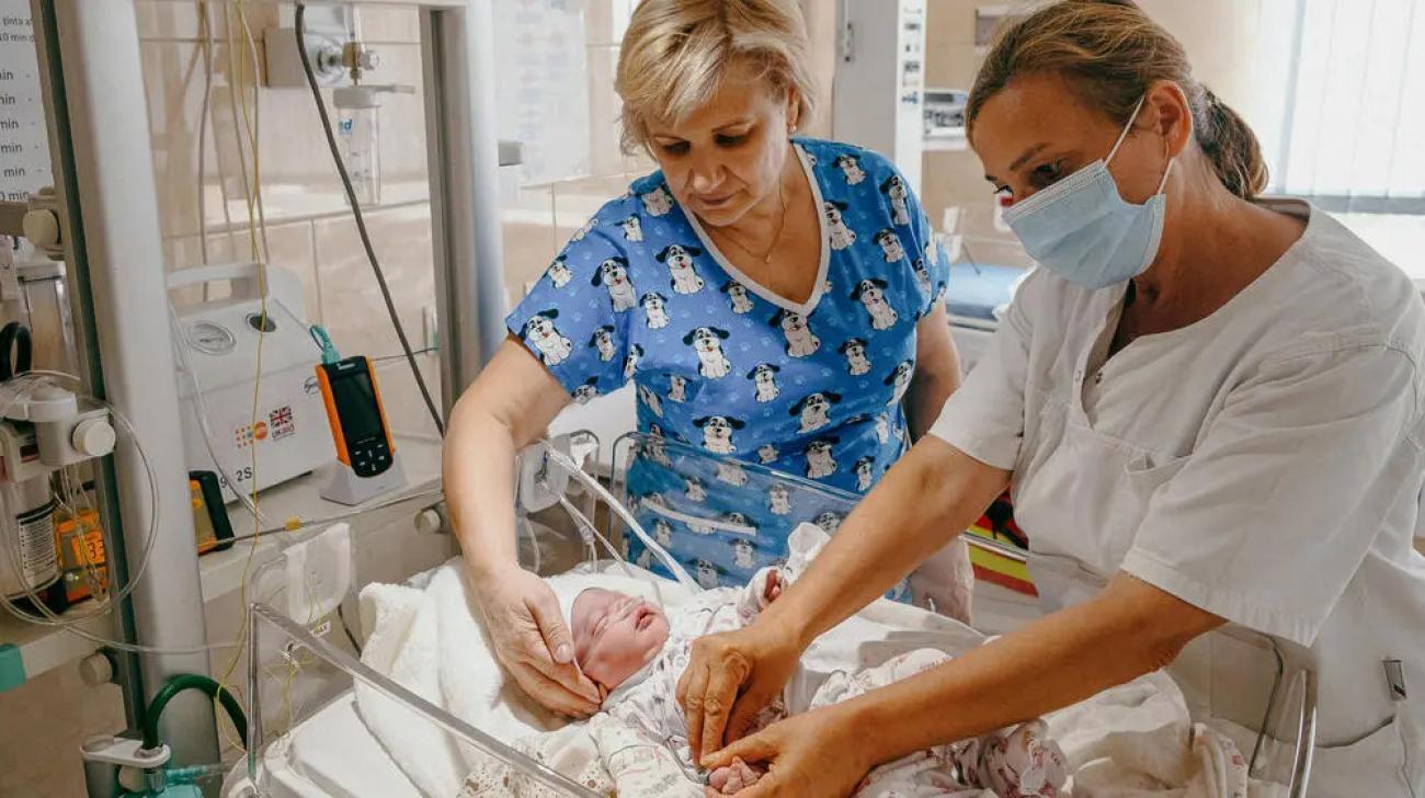 Two nurses care for a child in a NICU