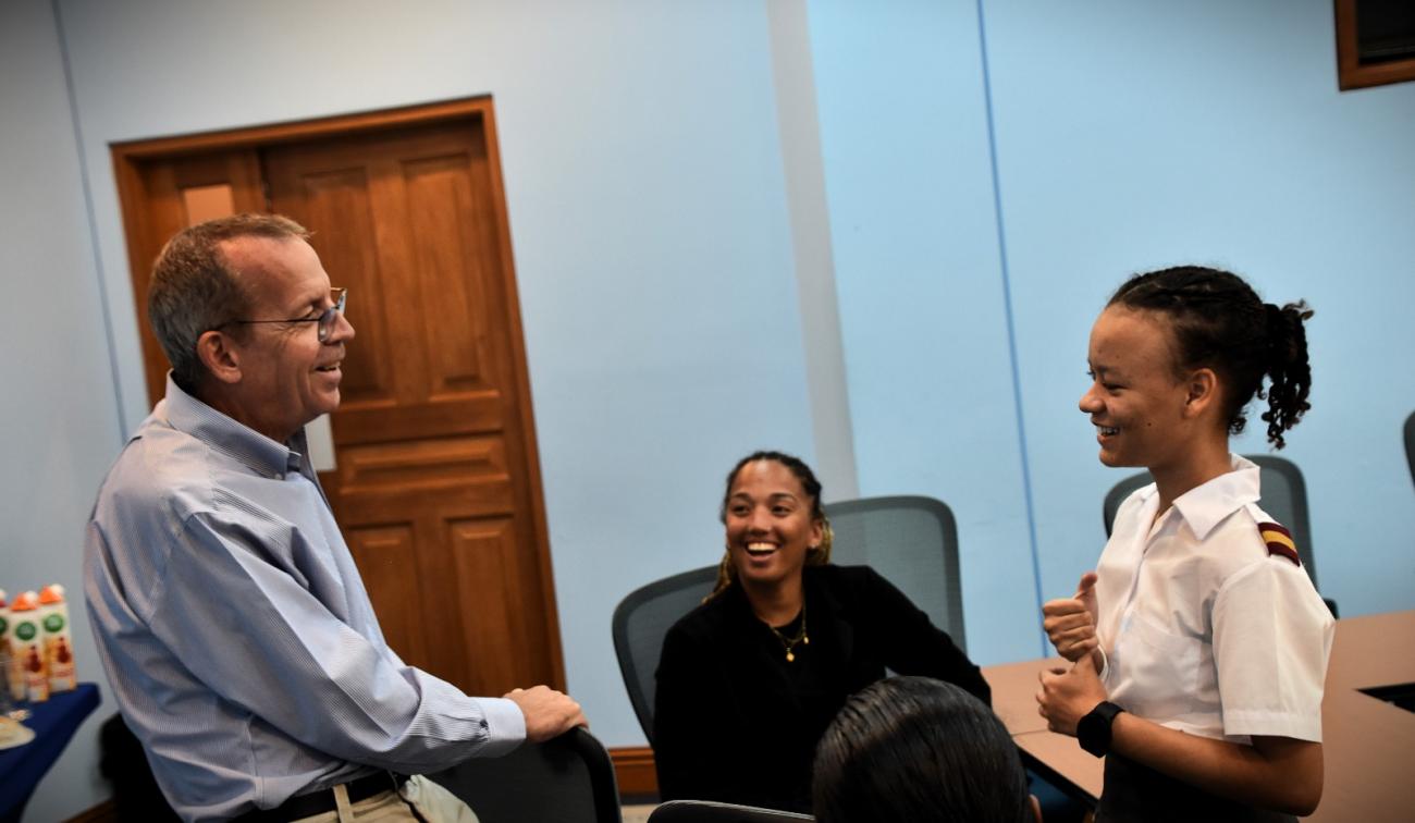A man in a light blue shirt, UN RC Simon Springett, smiles as he talks to two young students