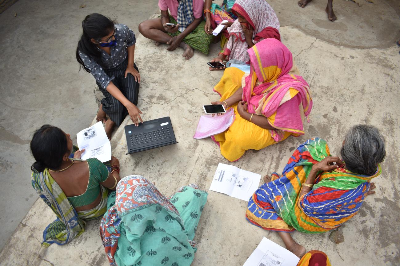 An aerial view of a group of women in colourful clothes, holding cell phones and a laptop
